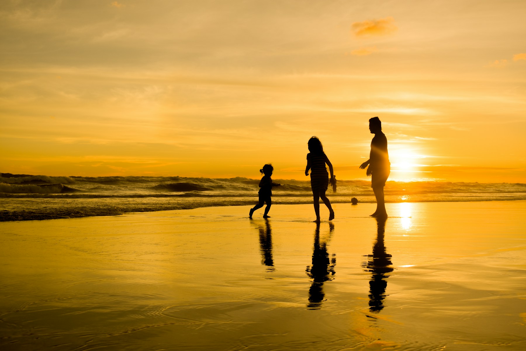 Família a caminhar na praia ao pôr do sol